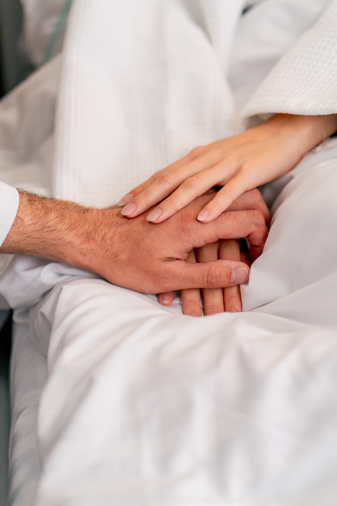 a male doctor's hand holding a female patient's hand on a bed in a hospital ward for moral support