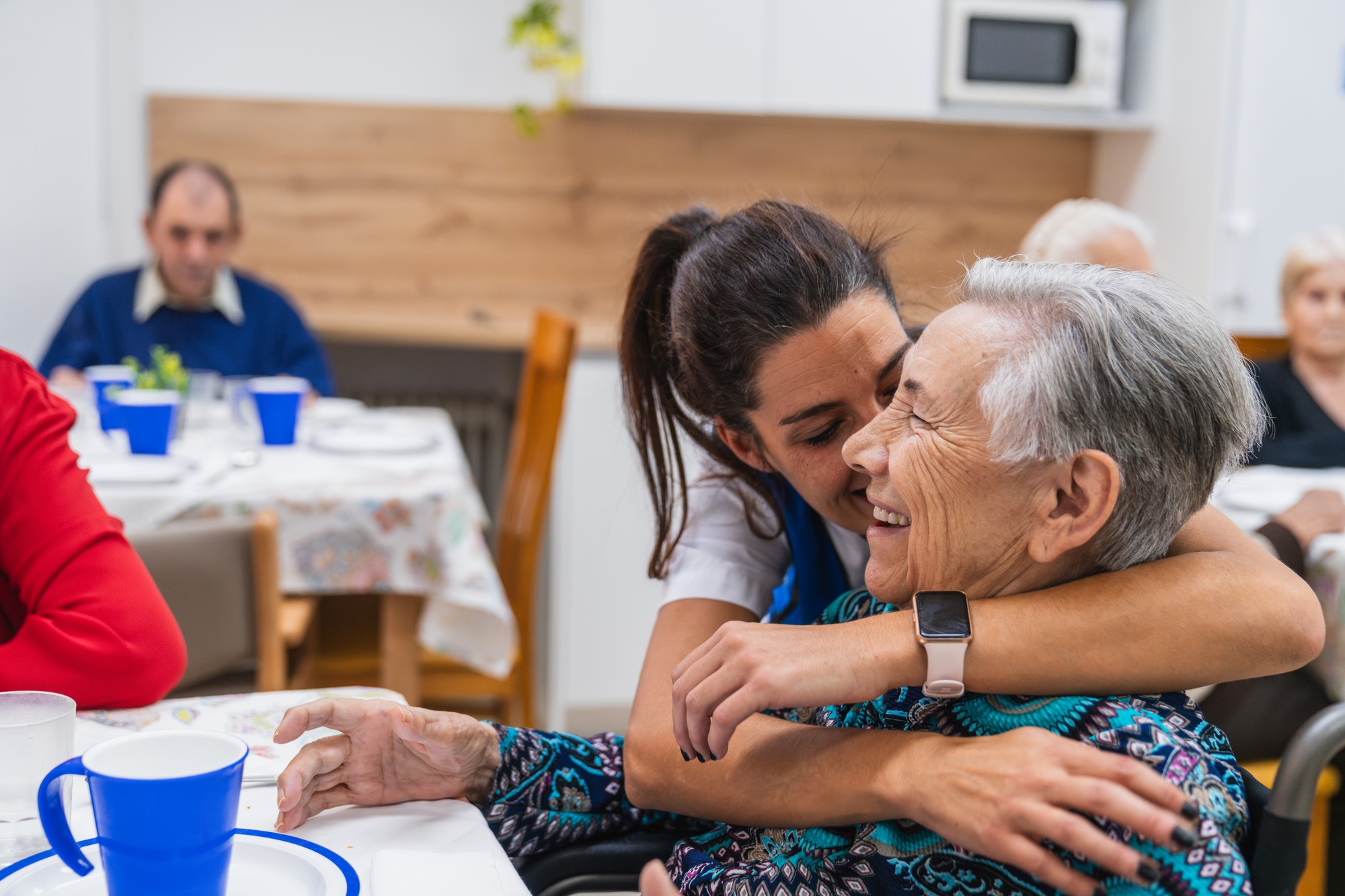 Caring nurse embracing elderly woman in nursing home